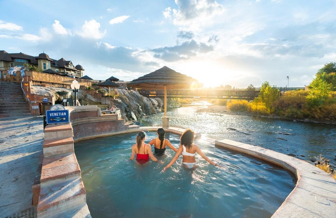 People enjoying the hot springs pool with scenic river and sunset view.