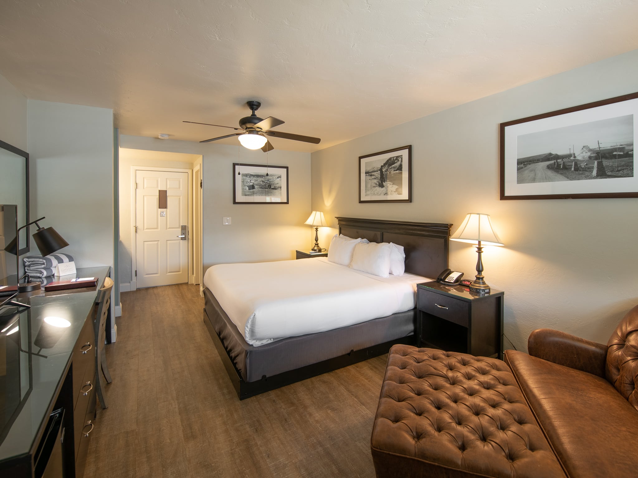 A king bed with white linens furnishes a hotel room. Light green walls, wood-look floor, a desk displaying a card reading 