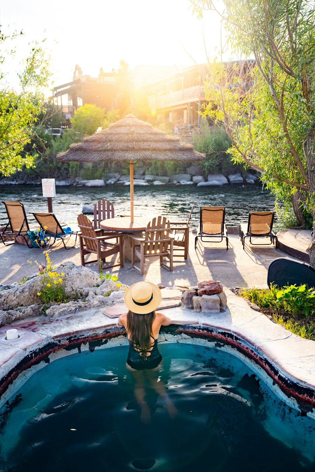 A woman in a straw hat relaxes in a hot tub on a sunny riverside patio with lounge chairs and a thatched umbrella.
Text: PRIVATE PROPERTY NO TRESPASSING VIOLATORS WILL BE PROSECUTED TO THE FULLEST EXTENT OF THE LAW BEWARE OF DOG