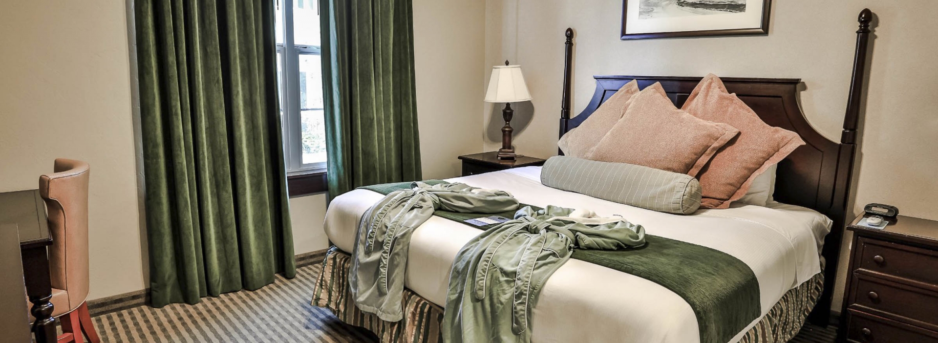 The bed between the two side tables with table lamps next to a large window with velvet curtains