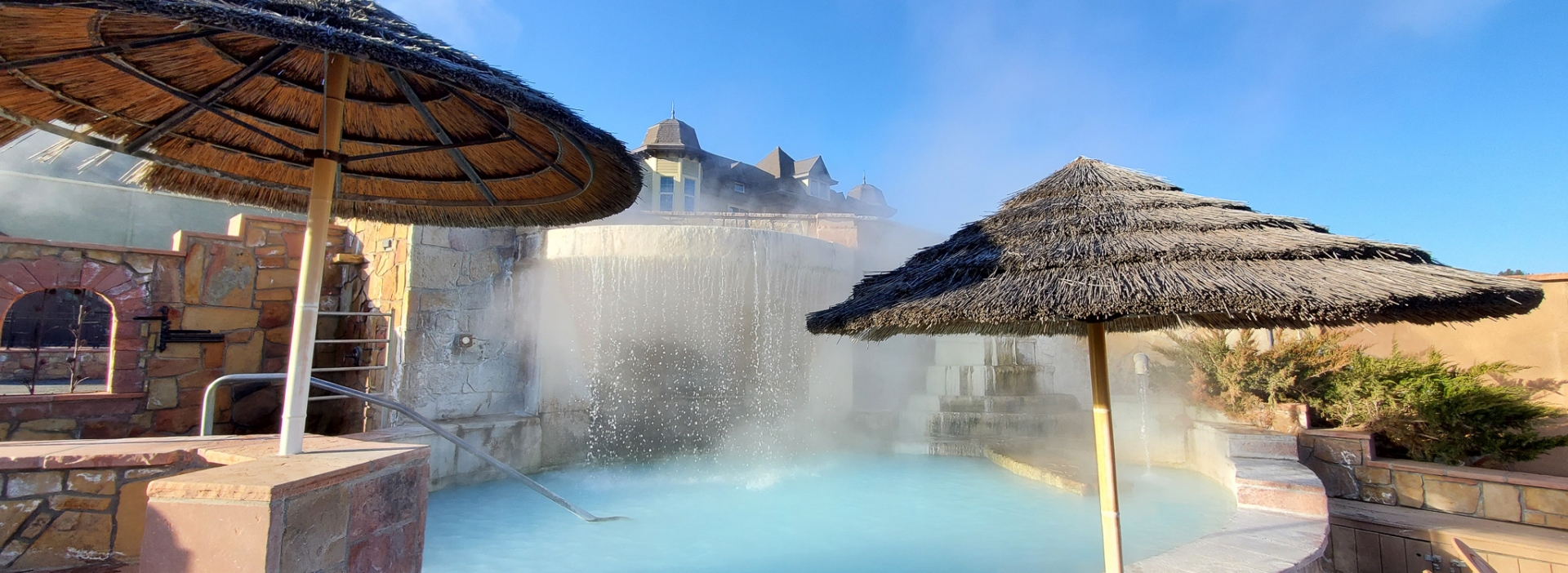 Waterfall filling the hot spring pool lined with thatched umbrellas