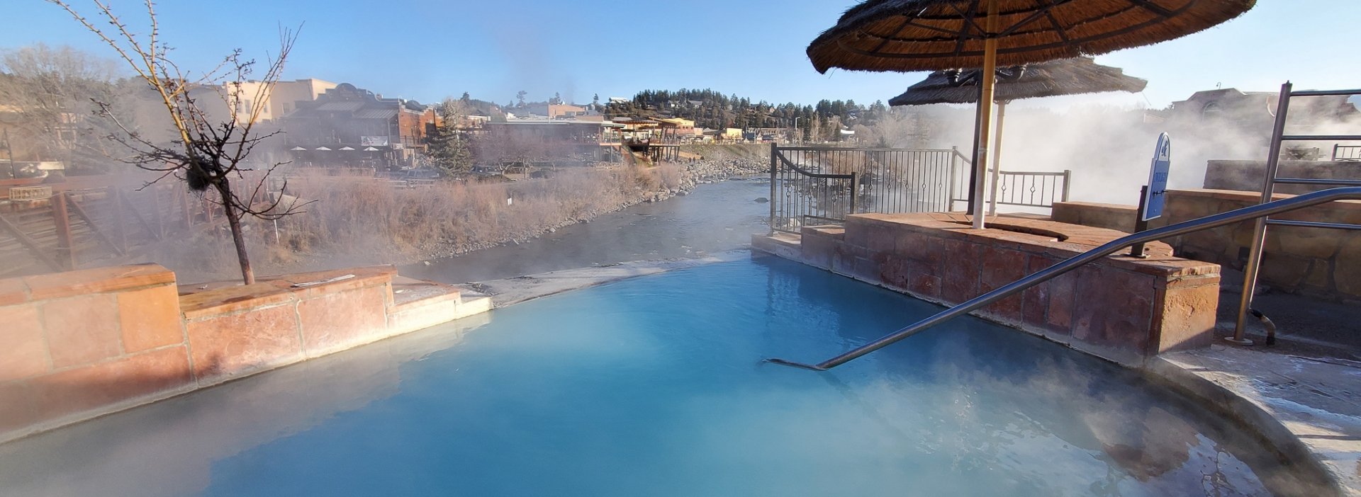 Steam rising from the hot spring pool with thatched umbrella and an outdoor view