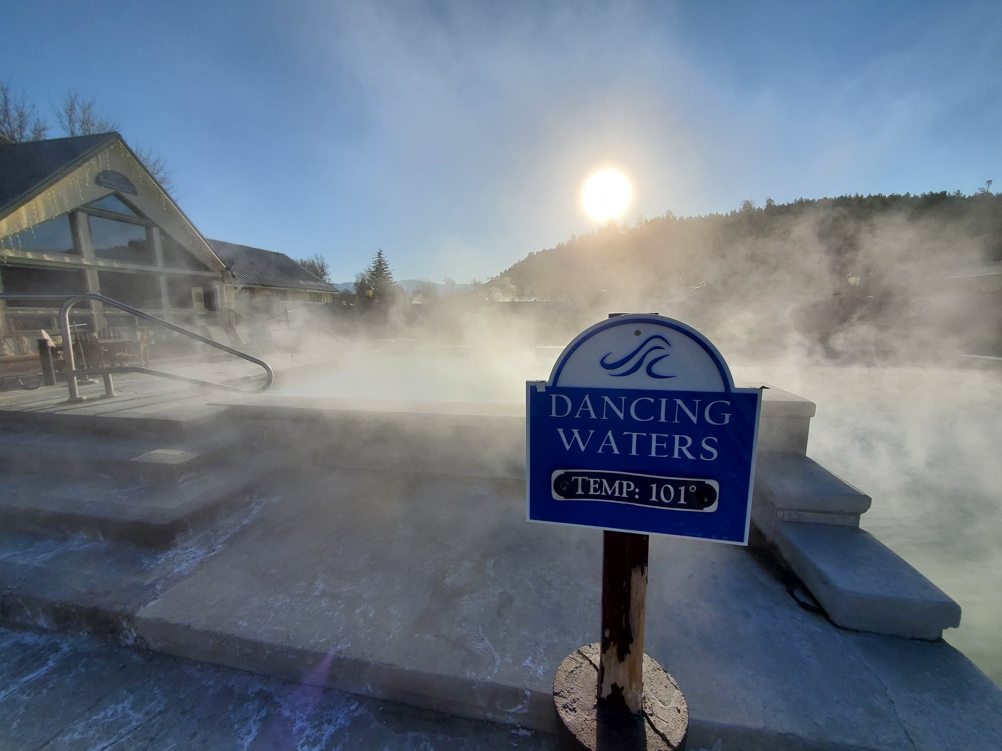 A blue sign stands beside a steaming pool, indicating 