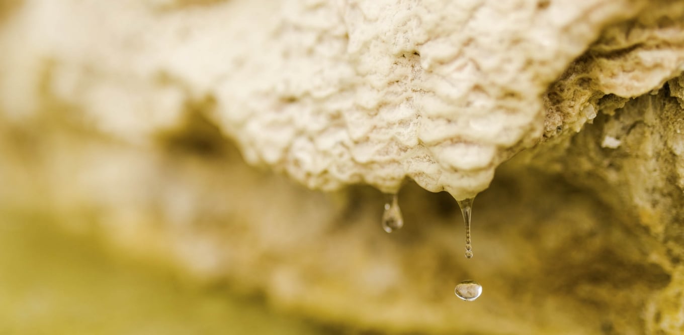 Water drops falling from a textured rock