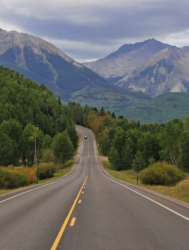 A wide shot of winding roads surrounded by trees and a view of the Colorado mountains