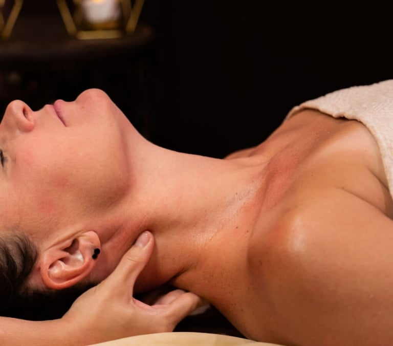 A woman lies eyes closed, receiving a neck massage, her skin reddened. Draped in a textured blanket, a dimly lit room with blurred candles forms the background.