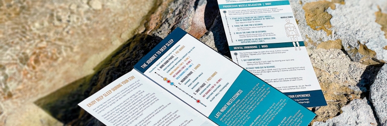 Two opened, blue and white brochures are lying on a textured, light-colored rocky surface, resembling natural stone, with subtle hints of water.
