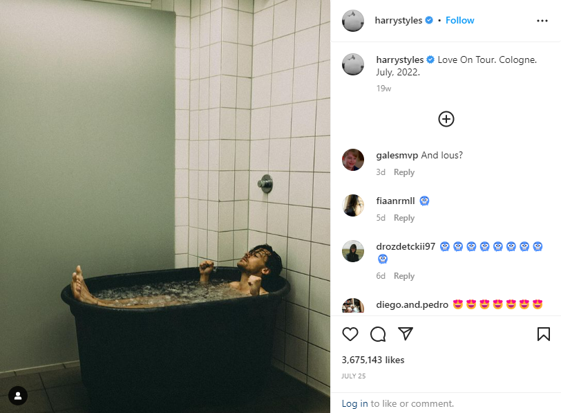 Harry Styles lies in a black ice bath, feet up and fists clenched, inside a tiled bathroom with a plain gray wall.