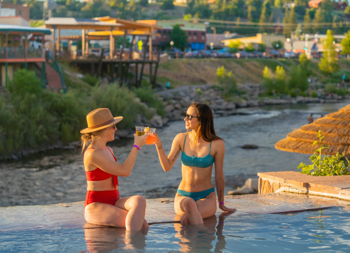 Two women in swimsuits, one with a hat, the other in 