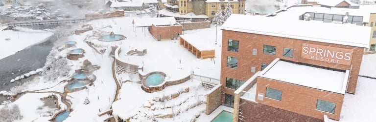 A snowy resort complex features numerous steaming outdoor hot tubs and buildings, including 