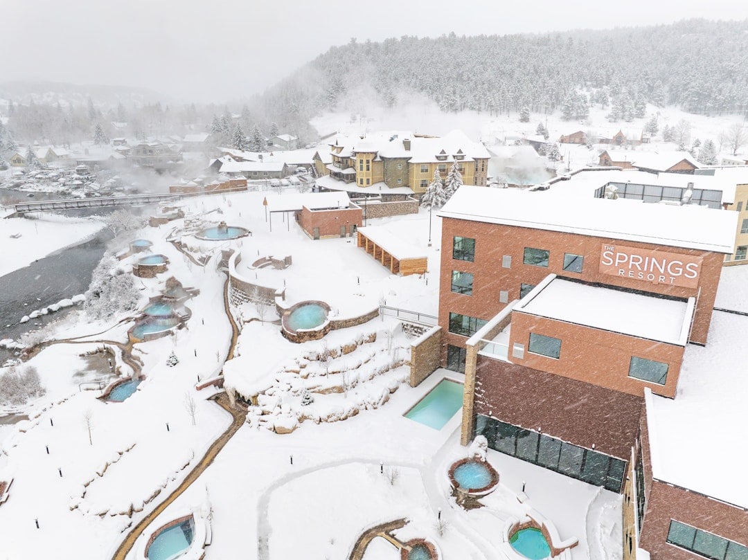 A snowy resort complex features numerous steaming outdoor hot tubs and buildings, including 