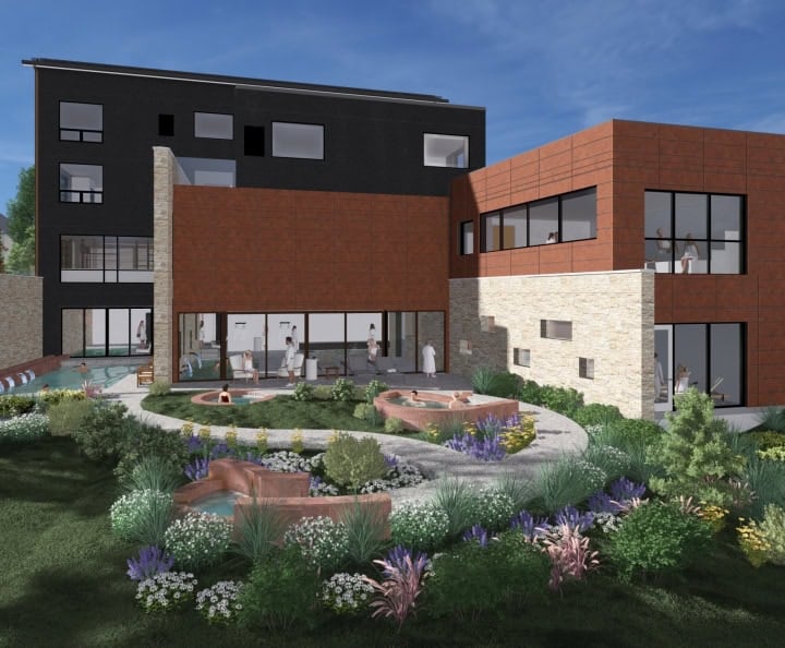 A modern multi-level spa building with dark, reddish-brown, and stone facades. Guests relax in outdoor soaking pools and inside, surrounded by lush gardens, pathways, and trees under a blue sky.