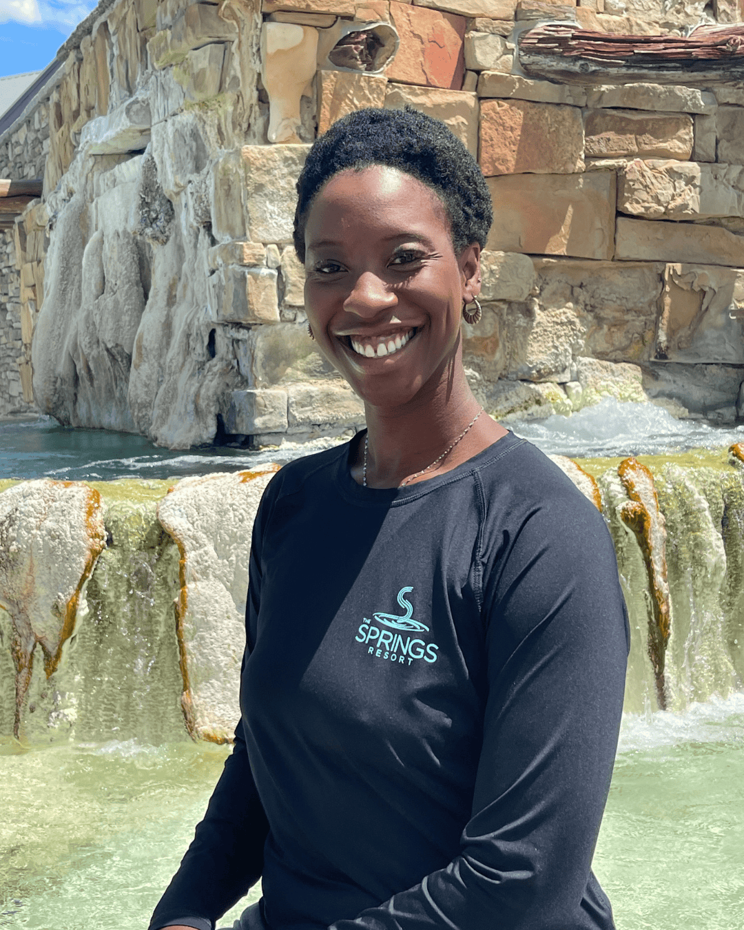Smiling woman in black Springs Resort shirt at hot springs waterfall in Pagosa Springs, CO.