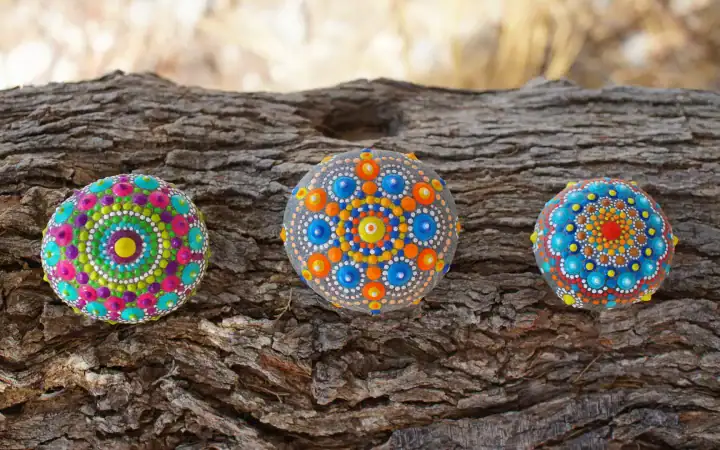Three painted rocks with mandala designs on a tree bark background.