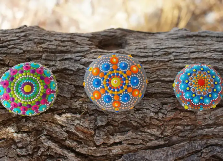 Three painted rocks with mandala designs on a tree bark background.