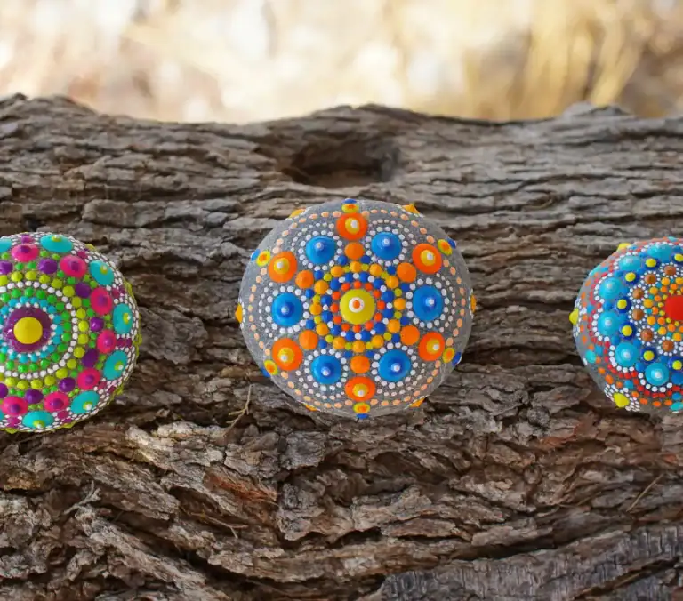 Three painted rocks with mandala designs on a tree bark background.