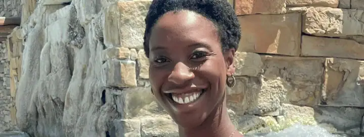 Smiling woman enjoying a morning soak at The Springs Resort with water and stone background.