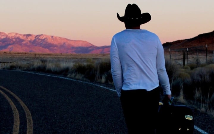 Person in cowboy hat walking with luggage at sunset near Pagosa Hot Springs.