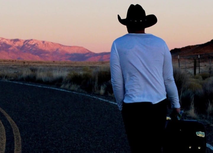 Person in cowboy hat walking with luggage at sunset near Pagosa Hot Springs.